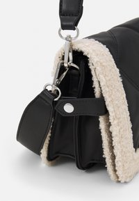 Svart läderväska med krämfärgad texturerad kant. Har en lås i silver med rem och har en slät, strukturerad form.