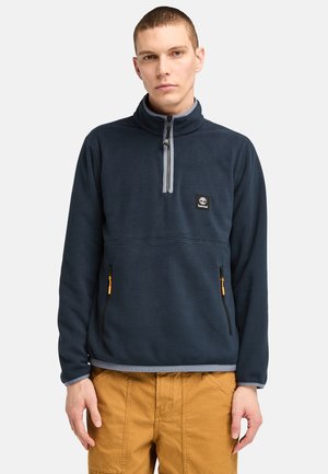 Marineblauer Fleece-Pullover mit halber Reißverschluss-Kragen, zwei vorderen Reißverschlusstaschen, grauen Akzenten und einem Logo-Patch auf der Brust. Weicher Stoff und lässige Passform.