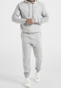 Gray sports sweatshirt with hood and drawstrings, featuring ribbed cuffs. Paired with matching joggers, both in soft, textured fabric.