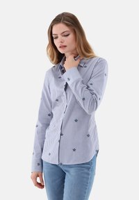 Button-up shirt in blue and white stripes, featuring small floral embroidery. Cotton fabric, long sleeves, standard collar, and tailored fit.