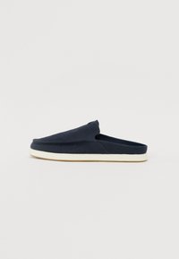 Mørkeblå slip-on sko laget av stoff med en teksturert overdel, avrundet front og en hvit gummisåle. Minimalistisk design uten synlig maskinvare.