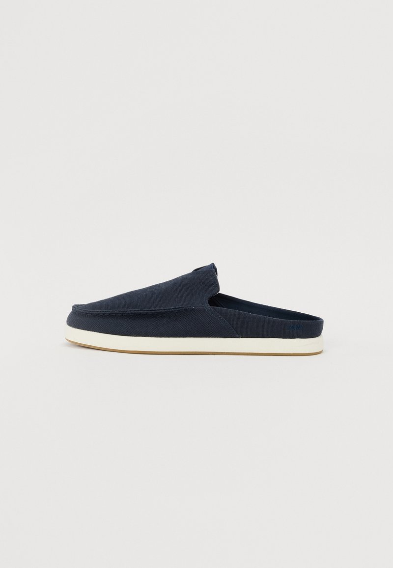 Mørkeblå slip-on sko laget av stoff med en teksturert overdel, avrundet front og en hvit gummisåle. Minimalistisk design uten synlig maskinvare.