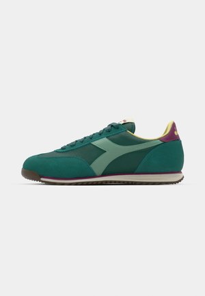 Green and teal athletic shoes with a suede and mesh upper, featuring a light green logo, yellow collar, and purple heel accent. Rubber sole.