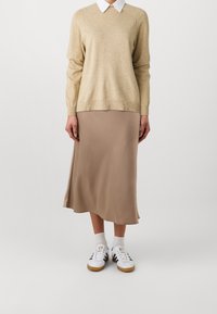 Beżowy sweter z okrągłym dekoltem na jasnobrązowej satynowej spódnicy midi, zestawiony z białymi sneakersami i białymi skarpetkami do kostek.