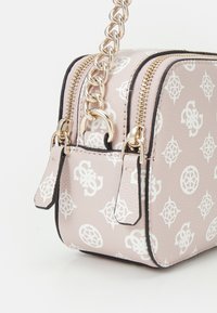Růžová crossbody taška z texturované umělé kůže s bílým vzorovaným designem, zlatými kovovými doplňky, dvojitým zipovým uzavřením a řetízkovým popruhem.
