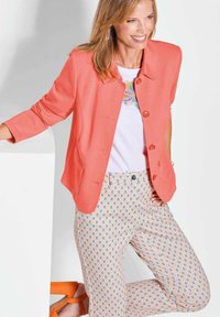 Koraal kleurige jas met driekwart mouwen en knopen aan de voorkant, gecombineerd met een broek met een patroon van druppelvormen in blauw en oranje accenten.