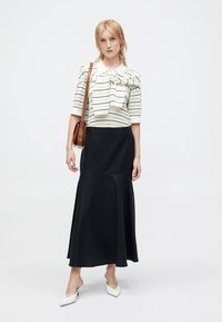 Bluză albă cu dungi negre orizontale și detaliu cu fundă, asortată cu o fustă midi neagră. Modelul poartă pantofi cu toc albi și o geantă maro tip crossbody.