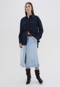 Mornarska srajca z gumbi in dvema žepoma na prsih, v kombinaciji z svetlo modrim jeans krilom z razporkom spredaj. Črne čevlje z visoko peto in naborki dopolnjujejo izgled.