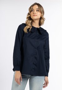 Marinblå skjorte med knapper, rynket krave, lange ærmer og en afslappet pasform. Stoffet ser glat og let ud.