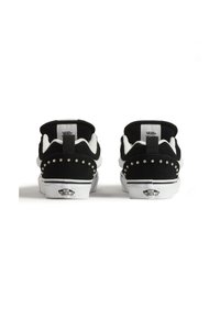 Zapatillas de ante negro con acentos blancos, que presentan detalles con tachuelas en el talón y una suela blanca de contraste, etiquetadas con la marca Vans.