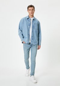 Camisa de mezclilla azul claro con botones y bolsillo en el pecho, utilizada sobre una camiseta blanca; combinada con jeans slim azul claro y zapatillas blancas.