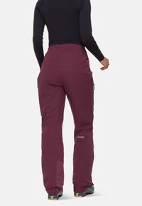 Vinröda skidbyxor med hög midja, sidofickor i cargo-stil och förstärkta ben. Har ett strukturerat material och varumärkeslogotyp på sidan.