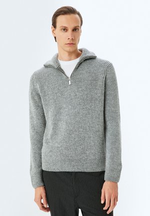 Suéter de punto acanalado gris con cuello de media cremallera, hecho de material suave. Presenta mangas largas y una cintura ajustada.