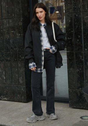 Czarna, oversize'owa kurtka, niebieska koszula w kratkę, biała koszulka, ciemne dżinsy i szare sneakersy. Gładkie tekstury w kontrastujących wzorach i kolorach.