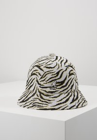 Gorra tipo cubo de Kangol con un tejido texturizado que presenta un patrón de cebra en negro, blanco y amarillo; logo bordado en la parte frontal.