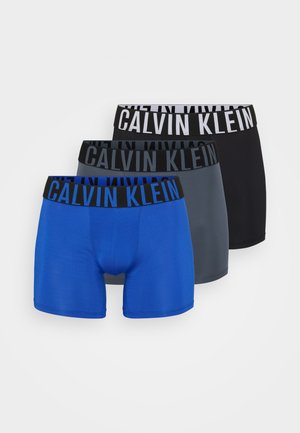 Drie paren boxershorts: één blauwe, één grijze en één zwarte, elk met een elastische CALVIN KLEIN tailleband met contrasterende tekst.