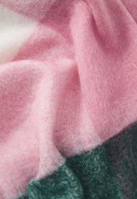 Blødt ternet stof i nuancer af pink og mørkegrøn med en fuzzy tekstur, der viser en blanding af farvegraderinger og tykkelse.