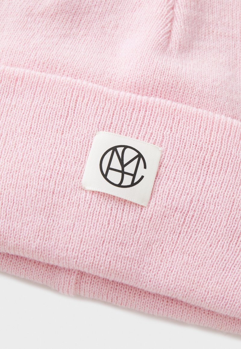 Różowa czapka beanie z dzianiny, wykonana z miękkiego materiału, z zawiniętym mankietem i białą metką z czarnymi detalami logo.