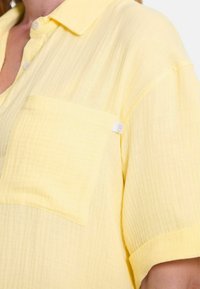 Geel kortlopende button-up shirt van lichtgewicht stof, met een borstzak en een textuur met een licht gekreukt uiterlijk.