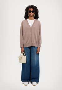 Beige oversized cardigan with button closure, paired with wide-leg blue jeans. Accessories include a small light beige handbag and dark sunglasses.