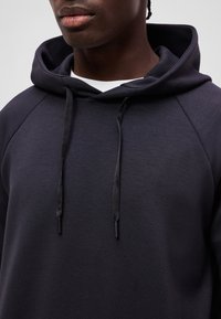 Close-up of a person wearing a dark navy hoodie with drawstrings and a white shirt underneath.