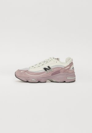 Lichtroze en witte New Balance sneaker met zwart logo, mesh- en suèdepanelen, dikke gevoerde zool en witte veters, zijaanzicht.