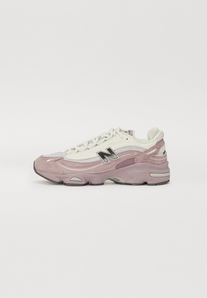 Baskets New Balance rose clair et blanc avec logo noir, panneaux en mesh et en suède, semelle épaisse rembourrée et lacets blancs, vues de côté.
