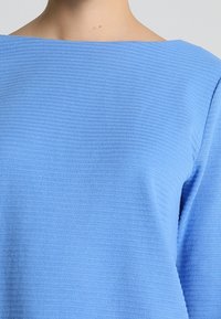 Hellblauer, strukturierter Pullover mit quadratischem Ausschnitt, aus weichem Material mit horizontalen Streifen. Die Ärmel sind lang und leicht lässig.