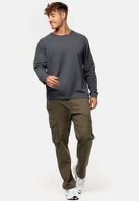 Graues langärmeliges strukturiertes Hemd, kombiniert mit olivfarbenen Cargo-Hosen mit großen Seitentaschen. Weiße Sneakers runden das Outfit ab.
