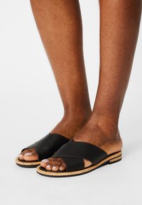 Sandales en cuir noir à enfiler avec un design à lanières croisées, semelle en liège et détails texturés sur le plateau. Style ouvert à l'avant.