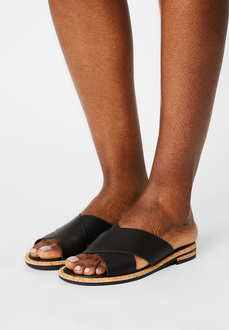 Sandales en cuir noir à enfiler avec un design à lanières croisées, semelle en liège et détails texturés sur le plateau. Style ouvert à l'avant.