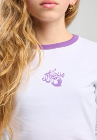 T-shirt bianco con un colletto a coste viola e un logo stampato "Cherish". Materiale in cotone morbido, design aderente.