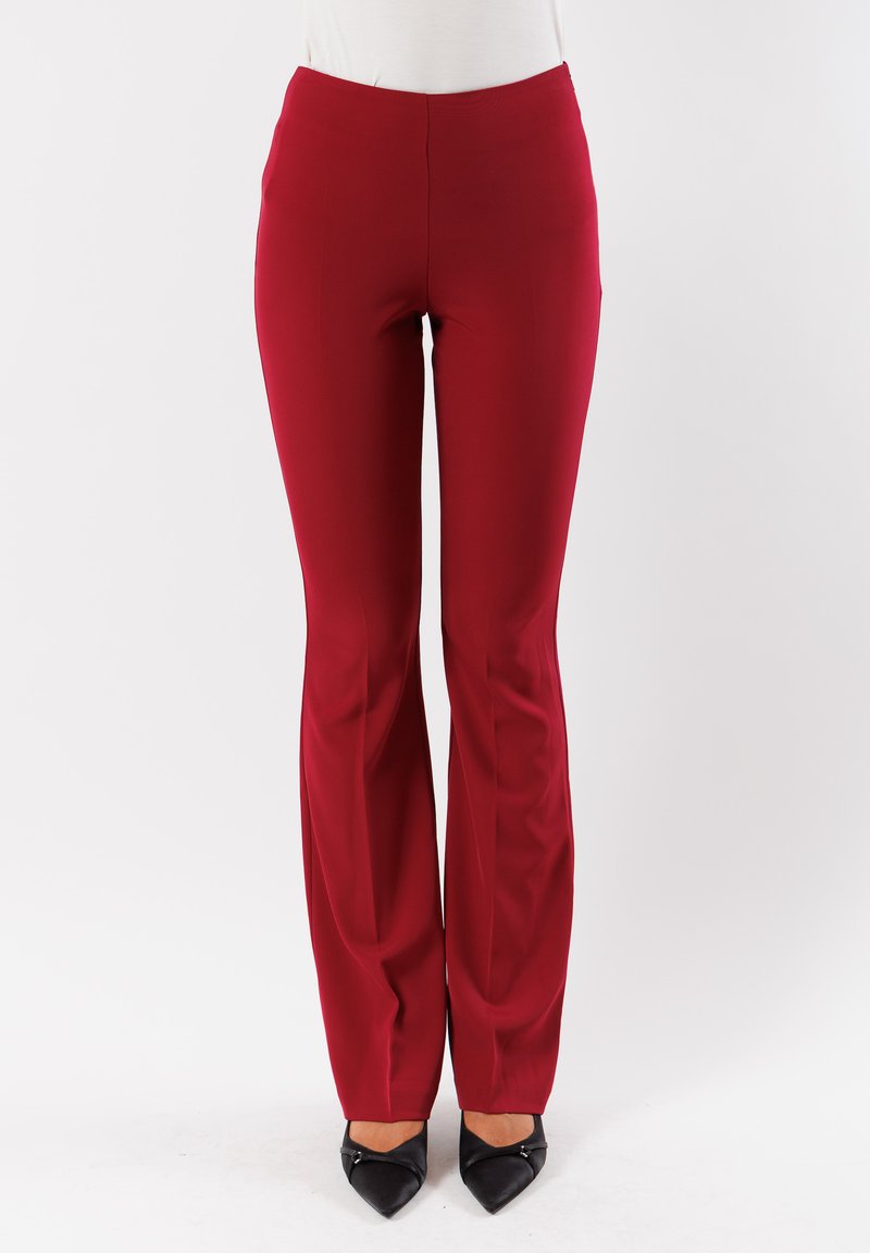 Pantaloni rossi aderenti con una texture liscia e un design a gamba dritta. Presentano un alta vita e un taglio a lunghezza completa, abbinati a tacchi neri.