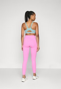 Ljusblå sport-bh med utskärningsdesign; rosa leggings med slät yta; vita löparskor. Bakifrån av modellen.