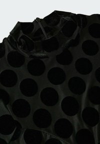 Czarna sukienka z dużymi czarnymi polka dotami z aksamitnego materiału na gładkim tle. Posiada wysoki kołnierz i zasłonięty zamek z tyłu.
