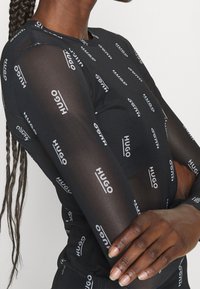 Schwarzes Langarmoberteil aus durchscheinendem Material mit wiederholtem weißen "HUGO"-Logo. Enganliegendes Design mit rundem Ausschnitt.