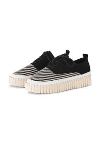 Zapatos de tela tejidos en blanco y negro con una suela crema estriada, que presentan un diseño de cordones y una parte superior suave con un patrón texturizado.