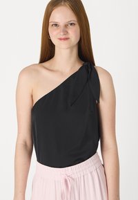 Svart sateng en-skulder topp med knytedetalj. Har en glatt tekstur og passer med lyse rosa bukser med elastisk midje.