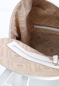 Interno di borsa bianca con fodera beige che presenta un motivo a logo ripetuto. Contiene una tasca con zip e una texture liscia.