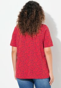 T-shirt rossa di cotone con un motivo grafico nero ripetuto. Maniche corte, vestibilità ampia e scollatura rotonda. Visualizzazione della parte posteriore.