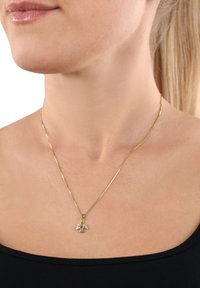 Collana d'oro con una catena delicata che presenta un piccolo pendente a forma di angelo adornato con gemme trasparenti, posato su pelle nuda.