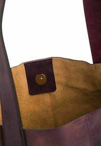 Intérieur d'un grand sac fourre-tout en cuir violet avec un bouton-pression doré. Extérieur lisse et doublure douce, semblable au daim, avec un léger éclat.
