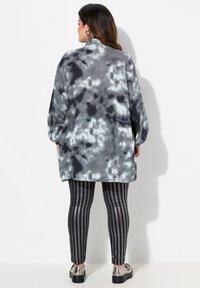 Overmaat grijze tie-dye top met een ontspannen pasvorm, gecombineerd met zwart en zilver gestreepte leggings en metallic schoenen. Soepele textuur en casual ontwerp.