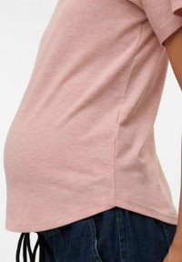 Närbild av en person som bär en rosa kortärmad topp och mörkblå denimbyxor, som framhäver sid sömmen och fållens detaljer.