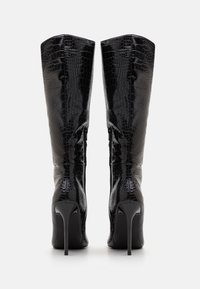 Bottes noires à talons hauts avec une texture en croco vernie, silhouette allongée et talon aiguille fin. Fermetures éclair sur le côté incluses.