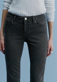 Jean en denim gris foncé à coupe slim, conception à cinq poches, fermeture par bouton argenté. Texture lisse avec une légère élasticité pour le confort.