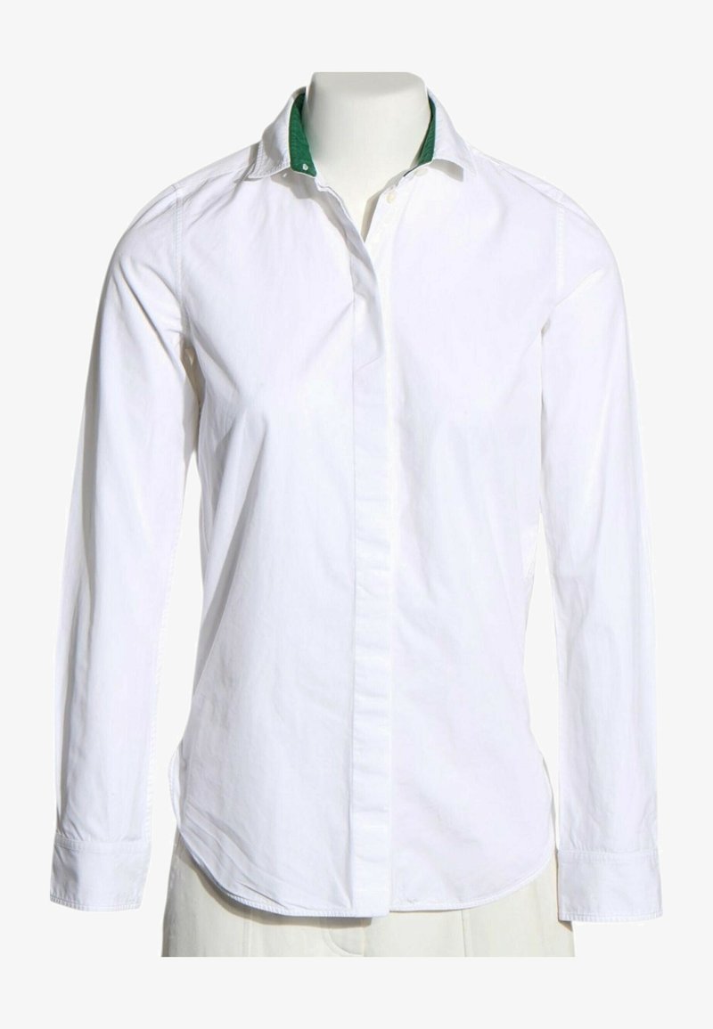 Chemise blanche à manches longues avec boutons cachés et col intérieur vert, présentée sur un buste de mannequin sur fond blanc.