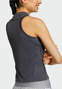 Sportski top bez rukava od tamnosive tkanine; ima visoki ovratnik, glatku teksturu i vertikalne rebraste detalje sa strane.