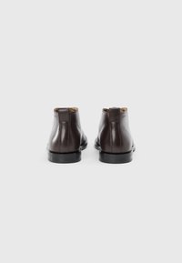Botas de cuero marrón hasta el tobillo con un acabado liso, punta redonda y suelas de goma negra. Presentan una lengüeta en la parte posterior. Diseño simple y minimalista.