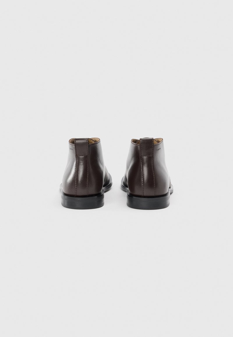 Bottines en cuir marron avec une finition lisse, bouts ronds et semelles en caoutchouc noir. Présente une languette à l'arrière. Design simple et minimaliste.